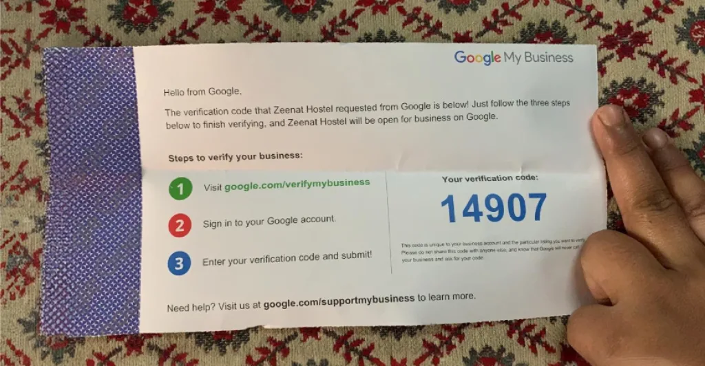 A hand holding a physical Google My Business verification postcard with a code.